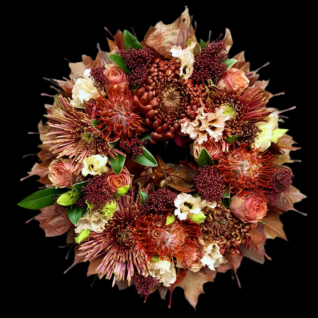 De krans is opgebouwd uit Leucospermum (speldenkussenprotea), Chrysanten, Rozen en Lisianthus, aangevuld met Skimmia ter opvulling.