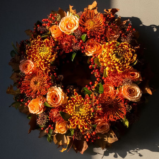 De krans is opgebouwd uit rode Leucospermum (speldenkussenprotea), rood-gele Chrysanten en oranje-roze Rozen, aangevuld met Skimmia ter opvulling