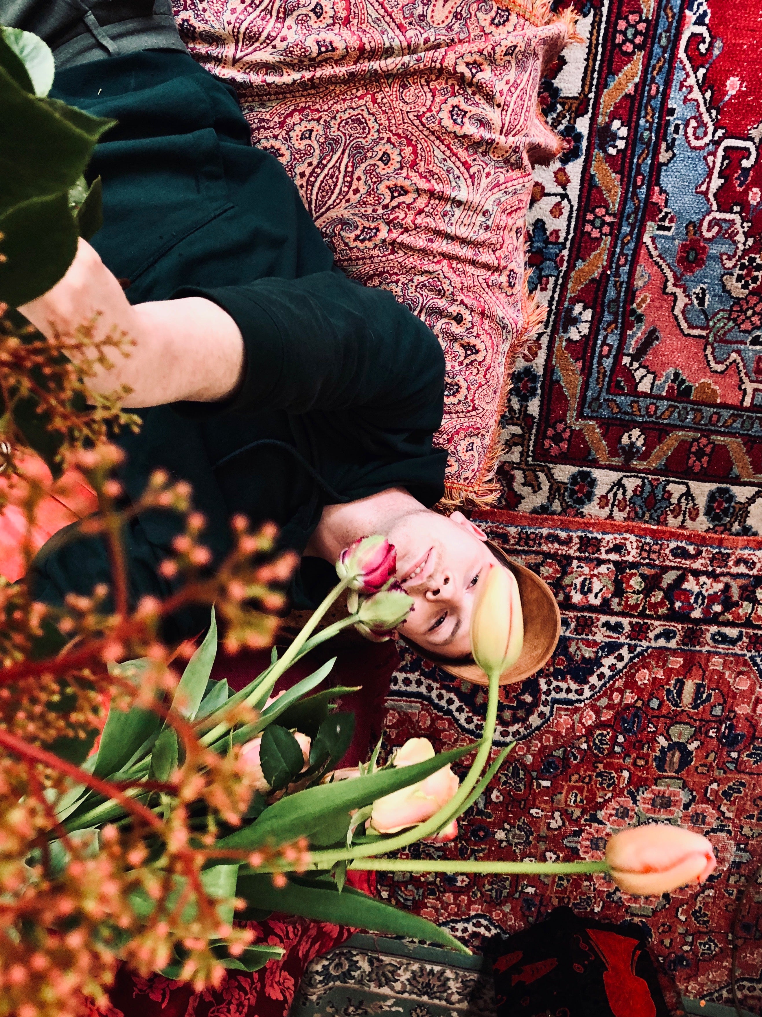 Profielfoto van florist Vincent Moens liggend op oosterse tapijten met tulpen op de voorgrond