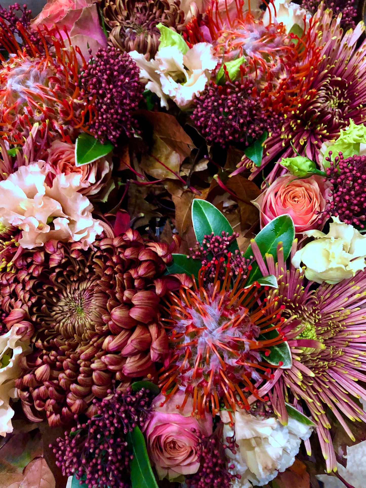 Detail van Allerheiligen bloemenkrans in herfsttinten gevuld met rozen, chrysanten, protea’s, bessen afgewerkt met herfstbladeren