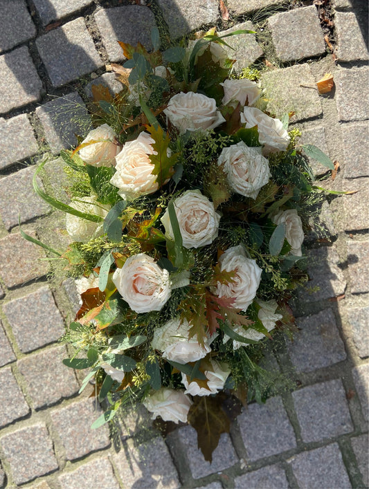 Klassiek Allerheiligen bloemstuk met licht gekleurde rozen en herfstbladeren en grassen als groenbasis