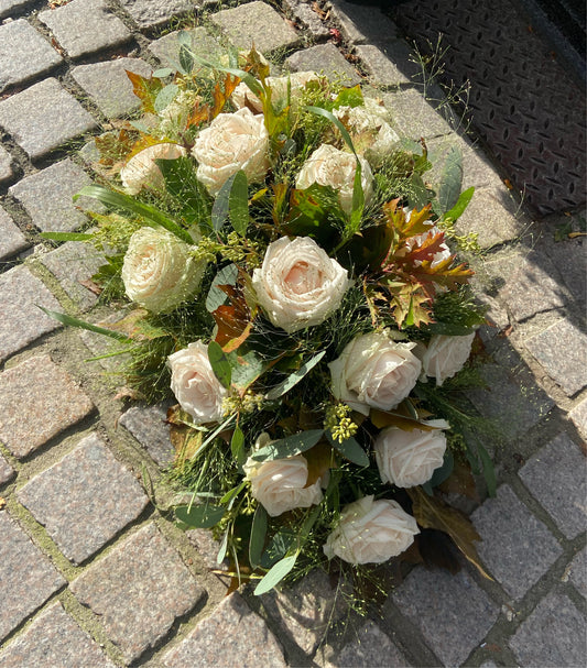Klassiek Allerheiligen bloemstuk met licht gekleurde rozen en herfstbladeren en grassen als groenbasis