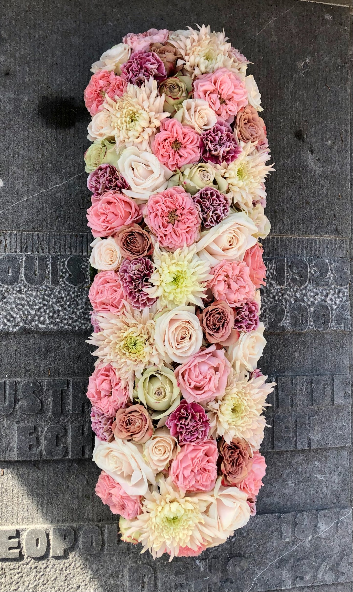 Langwerpig grafstuk met afgeronde hoeken voor Allerheiligen in zachte pasteltinten van een bloemen mix zoals rozen, chrysanten, anjers, tuinrozen
