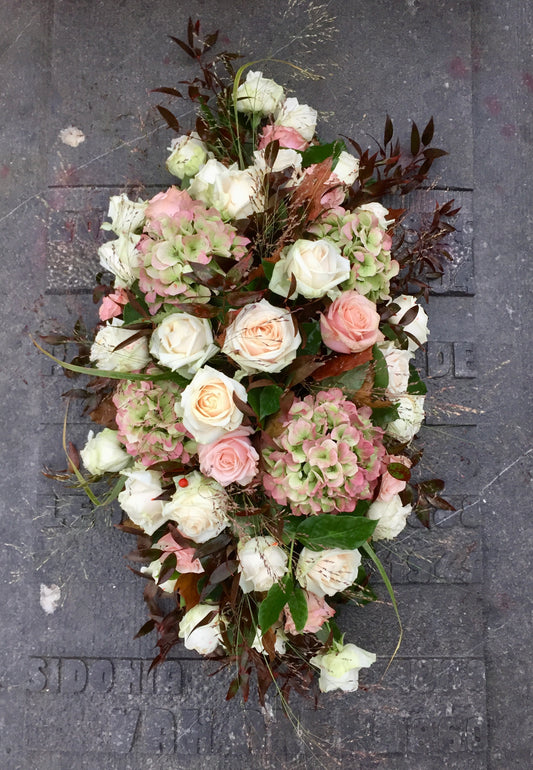 Langwerpig ovaal bloemstuk voor Allerheiligen in Herfstkleuren gevuld met rozen, hortensia, grassen en herfstbladeren