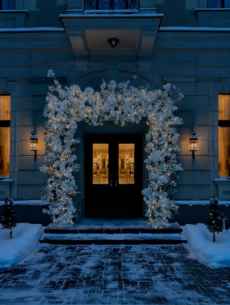 Gevelaankleding rondom de deur met witte bloemen en kerstlampjes