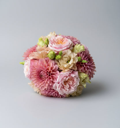 Rond gebonden bloemstuk met dicht op elkaar gestoken rozen, dahlia's of chrysanten en lisianthussen