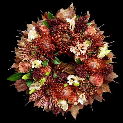 De krans is opgebouwd uit Leucospermum (speldenkussenprotea), Chrysanten, Rozen en Lisianthus, aangevuld met Skimmia ter opvulling.