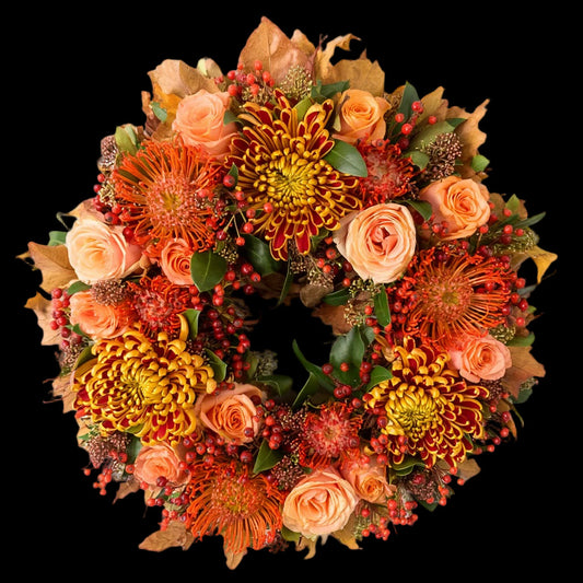 De krans is opgebouwd uit rode Leucospermum (speldenkussenprotea), rood-gele Chrysanten en oranje-roze Rozen, aangevuld met Skimmia ter opvulling