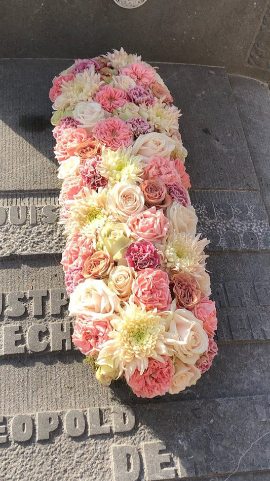 Langwerpig afgerond grafstuk voor Allerheiligen in zachte pasteltinten van een bloemen mix zoals rozen, chrysanten, anjers, tuinrozen